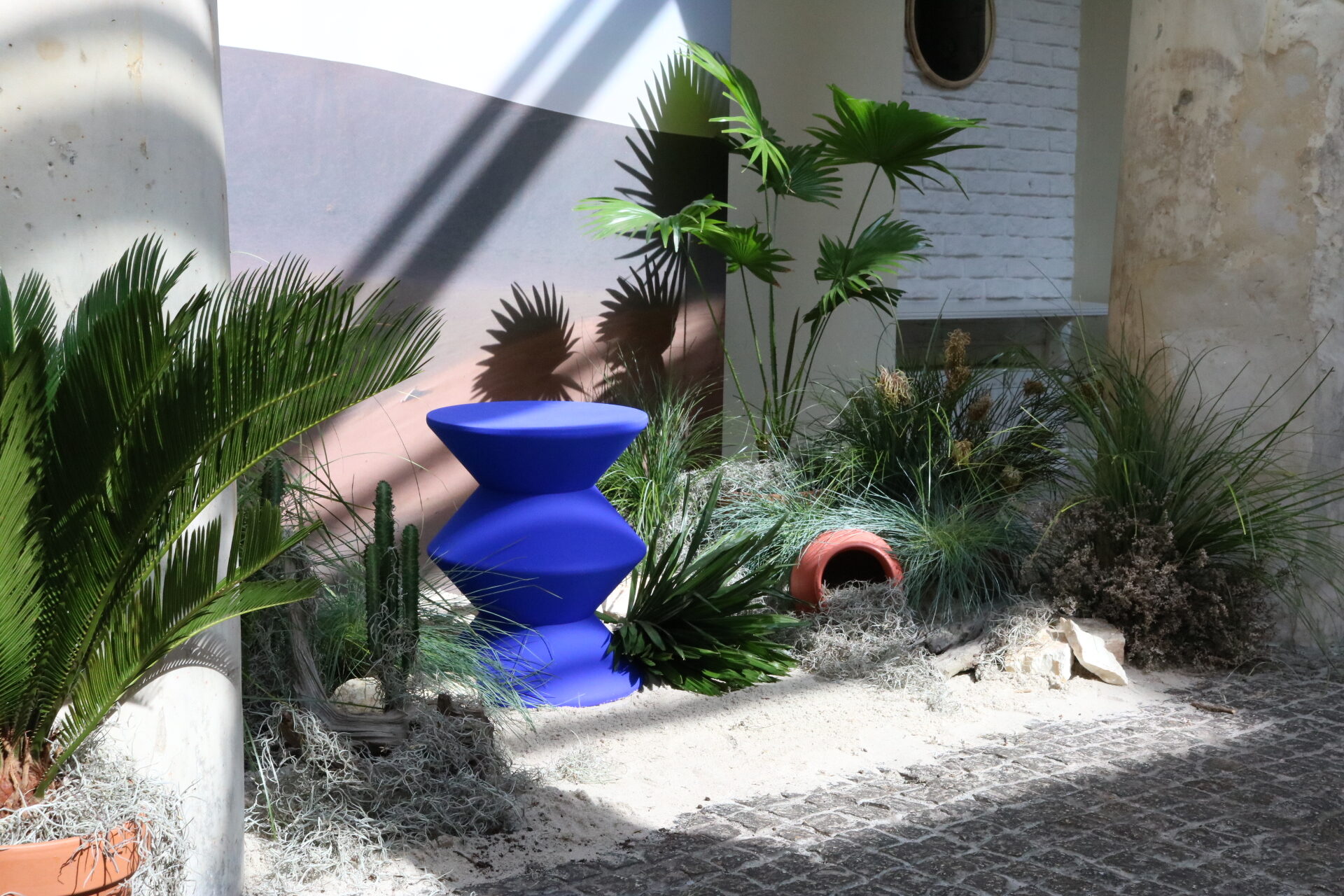 Niebieski geometryczny stołek na piaszczystej, pustynnej instalacji na Patio